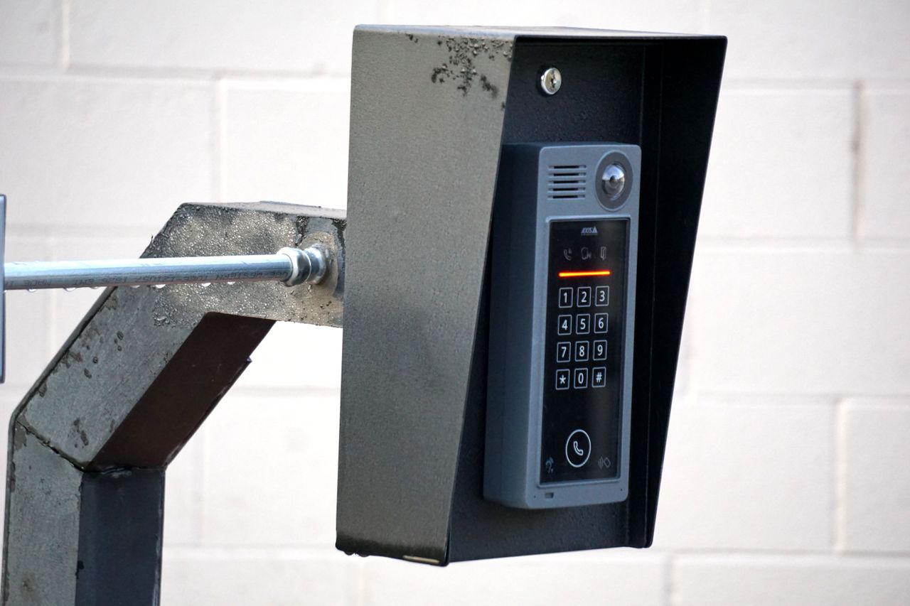 services-02 Close-up of a modern security intercom and keypad mounted on a wall outdoors with visible wiring.